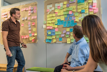 Colleagues discussing with sticky notes at wall in office