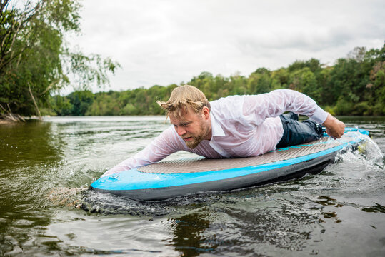Wet businessman lying on SUP board on a lake
