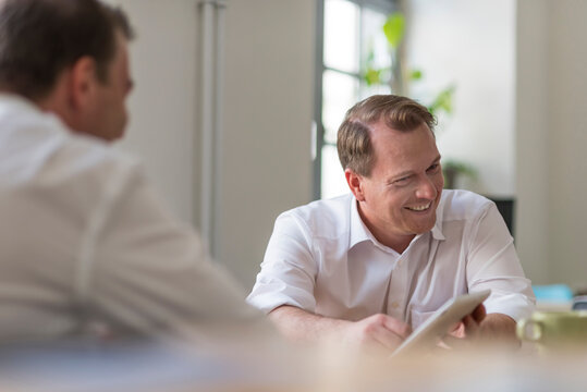 Two smiling businessmen working with tablet in office