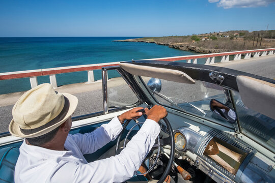 Taxi driver driving a vintage convertible car at the coast on Cuba