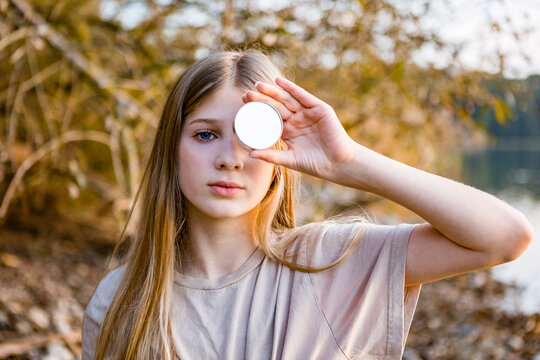 Portrait of girl holding mirror in front of eye during sunset