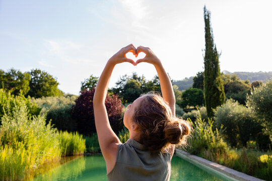 Rear view of a girl standing at swimming pool, forming a heart with her hands