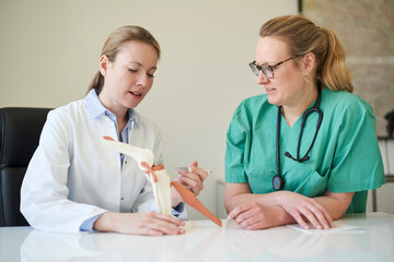 Female doctor and woman in scrubs with knee joint model talking