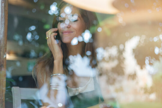 Young woman on cell phone behind windowpane of a cafe
