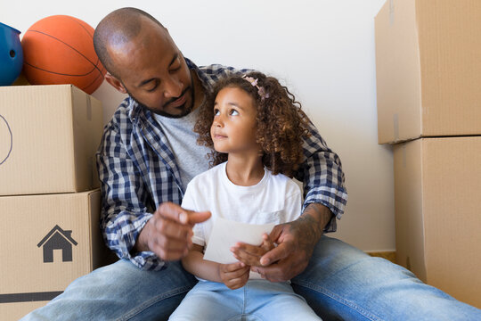Father and daughter sitting on the floor at new home surrounded by cardboard boxes