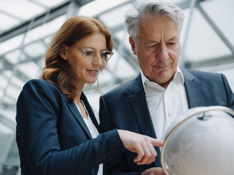 Businessman and businesswoman looking at globe in office