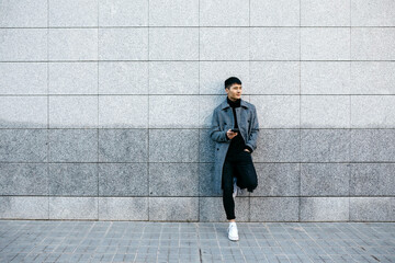 Young man with mobile phone leaning against wall waiting