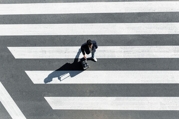 Man on zebra crossing pushing his trolley bag, top view