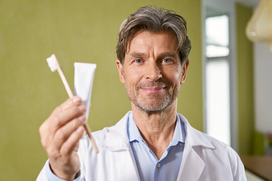 Portrait of dentist holding toothbrush and toothpaste in his medical practice