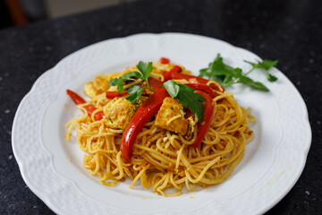 A Close-up of part of rice noodle dish with soy sauce, curry, red bell peppers, parsley and tofu. Vegan food. No people.