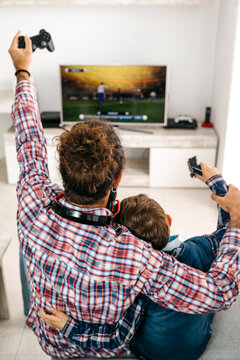 Back view of happy father and son sitting together on the couch playing computer game