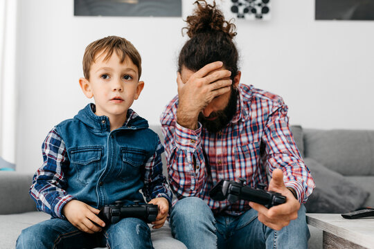 Father and son sitting together on the couch playing computer game