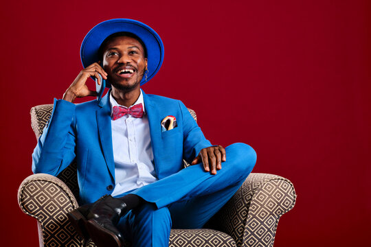 Laughing man talking on smart phone while sitting on chair against red background