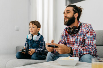 Portrait of father and son sitting together on the couch playing computer game