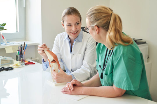 Female doctor and woman in scrubs with knee joint model talking