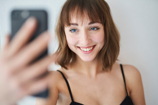 Portrait of smiling young woman taking selfie with smartphone at home