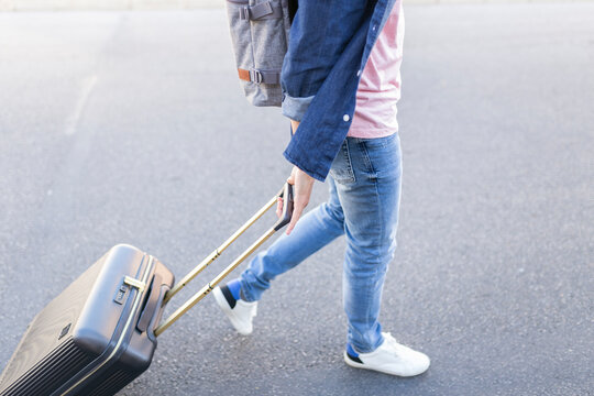 Crop view of man with backpack pulling trolley bag