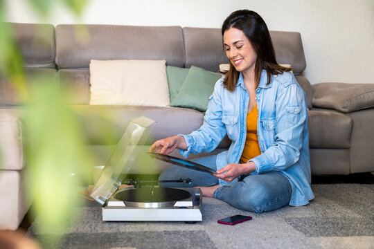 Smiling woman with turntable holding record while sitting by sofa at home
