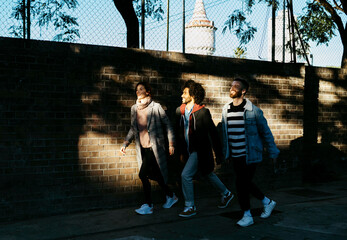 Three happy friends walking along a brick wall in shadow