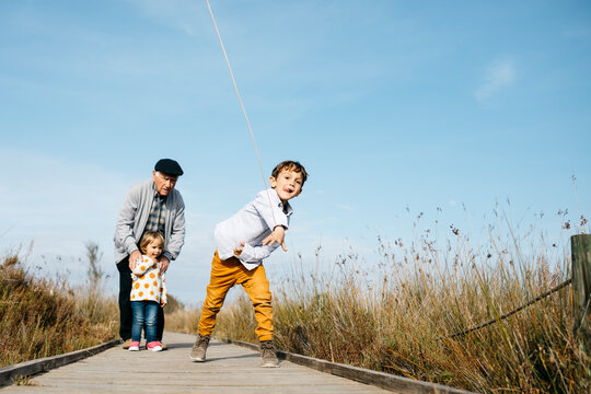 Boy on boardwalk throwing stick while his grandfather and his little sister watching him from the background