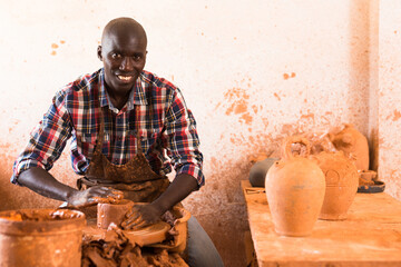 Skilled african american potter working on potters wheel making clay products in pottery workshop