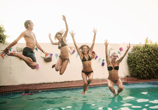 Carefree friends jumping together into swimming pool against sky during sunset - Powered by Adobe