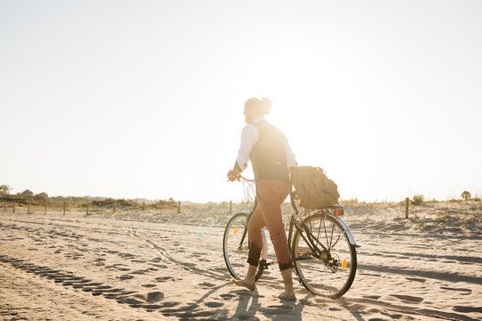 Well dressed man walking with his bike on a beach at sunset
