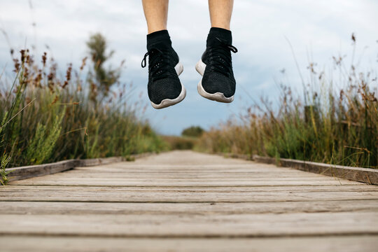 Black running shoes, male jogger jumping on a wooden walkway
