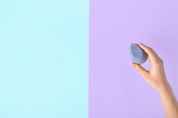 Female hand with stylish makeup sponge on color background