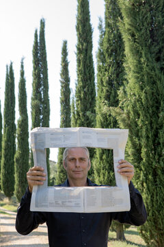 Italy, Tuscany, man surrounded by cypresses reading newspaper with a hole