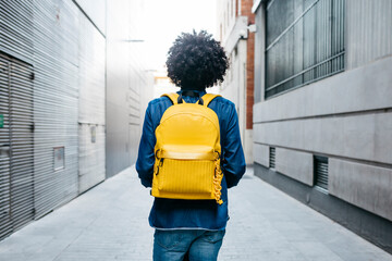 Back view of young man with yellow backpack on E-Scooter in the city