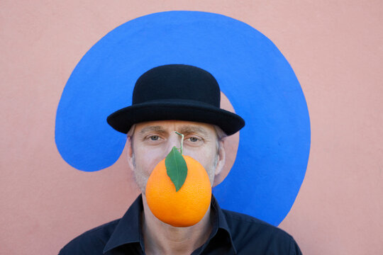 Portrait of man with an orange at a wall with question mark wearing a bowler hat