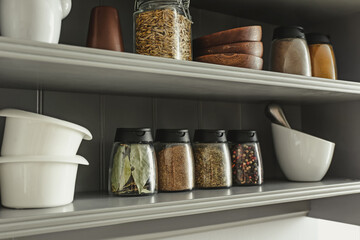 Jars with different spices and kitchen utensils on shelves