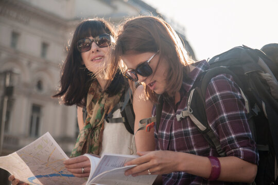 Women on vacation reading map while sitting at town square