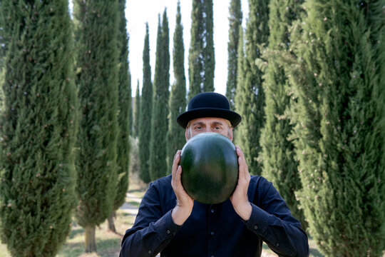Italy, Tuscany, man surrounded by cypresses wearing a bowler hat holding a melon
