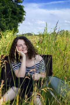 Portrait of happy young woman sitting in suitcase on a meadow looking at distance