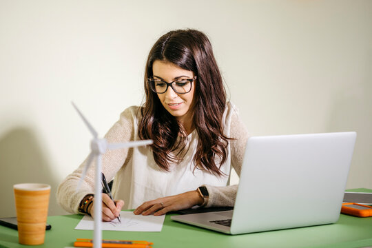 Young woman sitting at desk in office drawing on paper