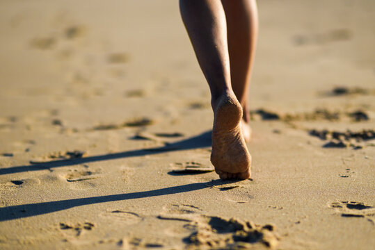 Close-up of woman's feet walking in sand on the beach