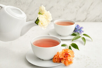 Tea pot and cups of hot beverage with flowers on table