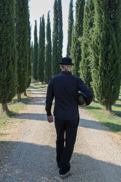 Italy, Tuscany, rear view of man surrounded by cypresses wearing a bowler hat holding a melon