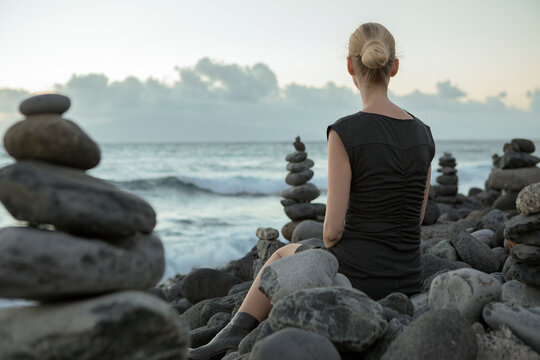 Spain, Tenerife, Costa Adeje, woman sitting between cairns at the coast
