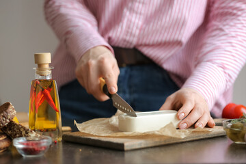 Woman cutting feta cheese on table in kitchen