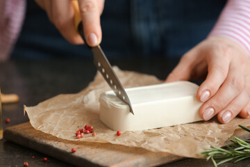 Woman cutting feta cheese on table in kitchen, closeup