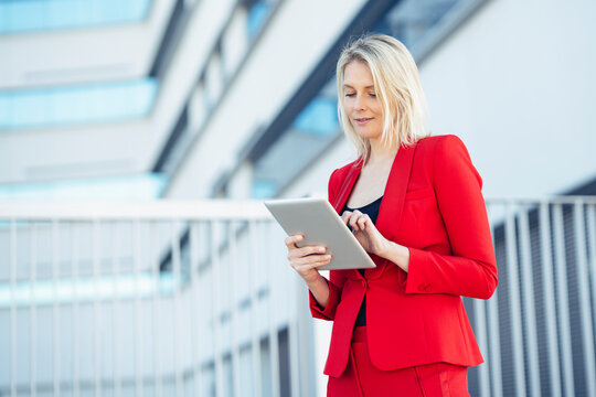 Blond businesswoman wearing red suit and using digital tablet at an office building