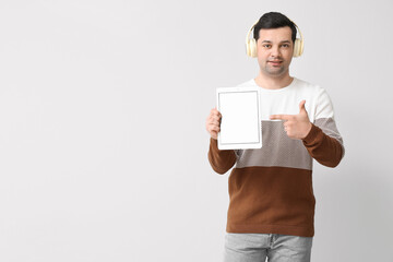 Young man with tablet computer and headphones on light background