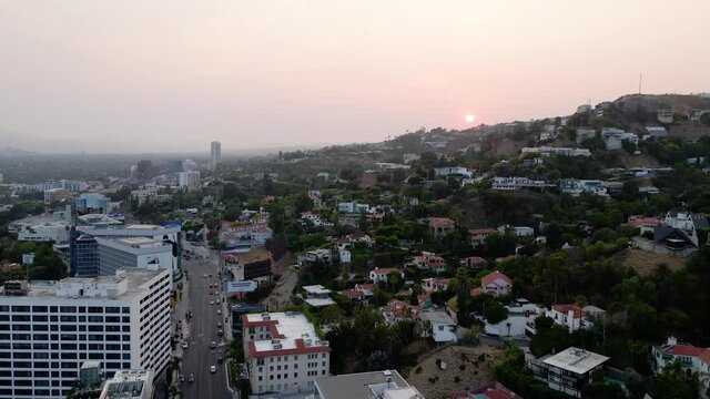 Aerial view of a sunset above a hillside neighborhood, the west Hollywood cityscape and the Los Angeles skyline background - pan, drone shot
