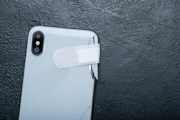 Broken mobile phone with medical plaster on dark background, closeup