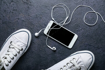 Mobile phone with broken screen, earphones and shoes on dark background