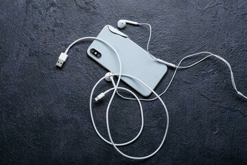 Broken mobile phone, charging cord and earphones on dark background