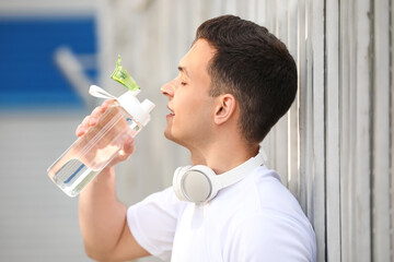 Fototapeta na wymiar Sporty young man drinking water after training at stadium